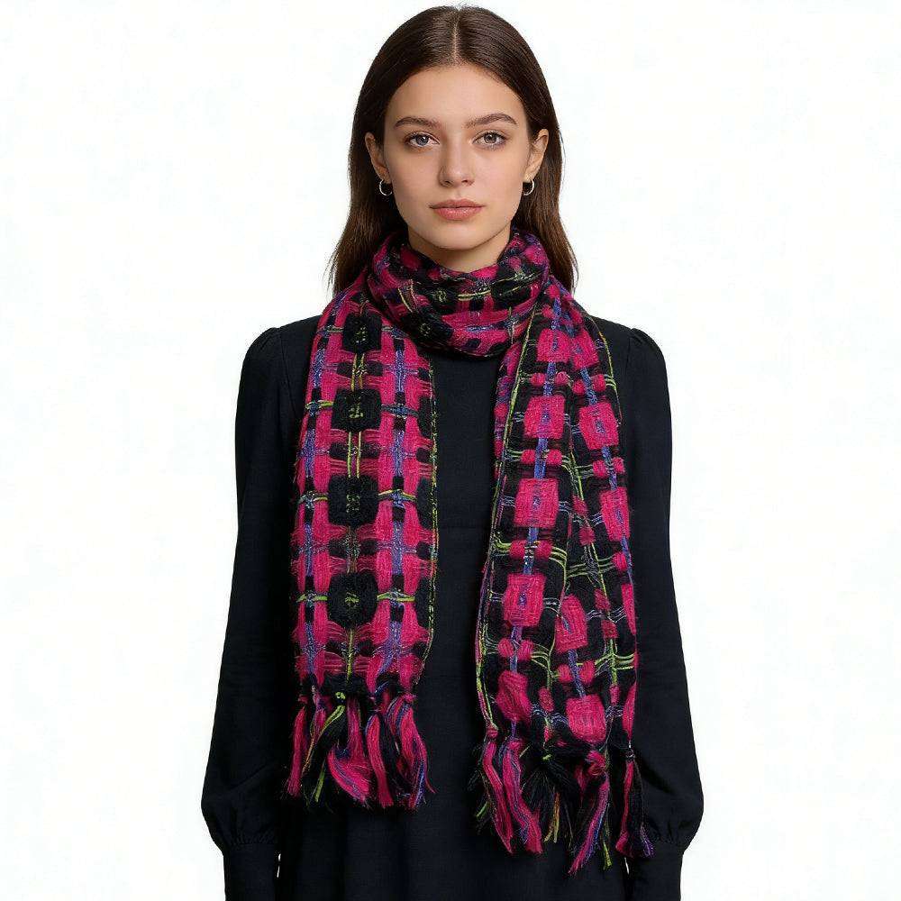 A stylish portrait of a young woman wearing a vibrant pink, black, and multicolored patterned scarf with fringe detailing over a simple black long-sleeve dress, showcasing a bold and elegant winter fashion accessory. | PicSEO 1775591636487