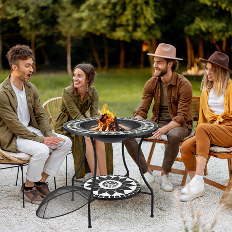 Four people sitting around a fire pit table in an outdoor setting with trees in the background.