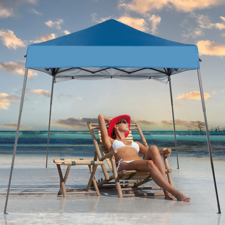 Woman relaxing on a beach chair under a blue canopy tent with ocean view.